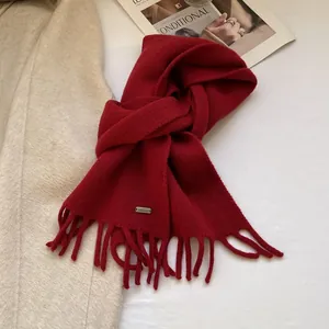 Close-up of a burgundy 100% wool knit scarf with tassels and a metallic logo plate