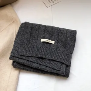 Close-up of dark grey cable knit wool scarf with 100% wool label on white surface