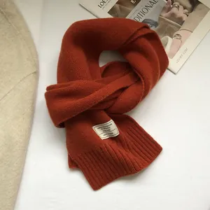 Macro detail of rust red 100% wool scarf showing ribbed knit texture and white fabric label