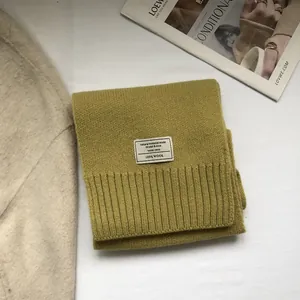 Detail view of mustard green 100% Australian wool scarf with fine knit texture and brand tag