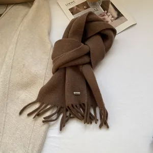 Detail of soft dark brown wool scarf featuring elegant tassels and a small silver logo plate