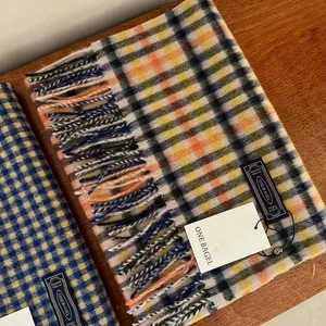Detail of warm orange and yellow plaid wool scarf featuring fringe and product tags