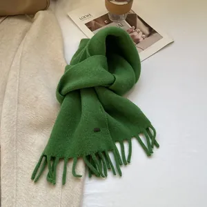 Close-up of grass green knitted wool scarf with long tassels and leather label detail