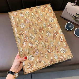 Dettaglio di sciarpa con foglie dorate accanto a una borsa e occhiali da sole chic