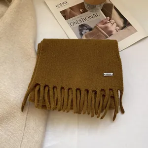 Detail showing 100% wool material tag and soft fringe texture on a mustard yellow scarf