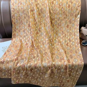 Dettaglio del motivo a foglie dorate su trama di sciarpa in lino e cotone beige
