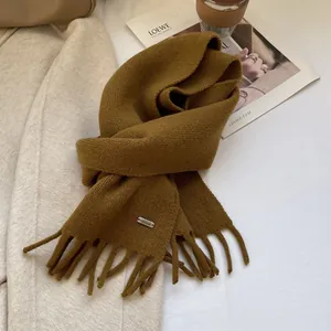 Macro detail of mustard yellow wool knit scarf with fringe and subtle metal brand plate