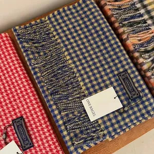 Detailed view of checkered wool scarves with fringe edges and brand labels on wood