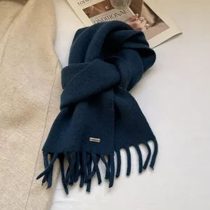 Close-up of navy blue wool knit scarf with fine tassel fringes and silver metal logo tag
