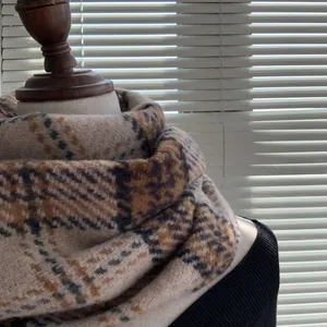 Détail du motif à carreaux marron et noir de l'écharpe sur un mannequin en bois