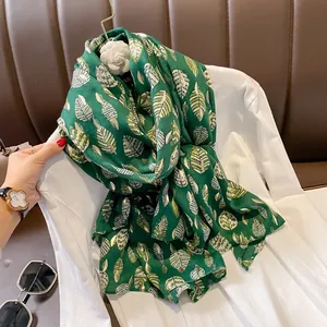 Dettaglio di sciarpa in lino verde scuro con motivi a foglia dorata su camicia bianca