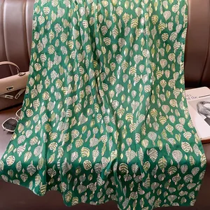 Dettaglio di sciarpa verde con foglie dorate su un elegante divano in pelle