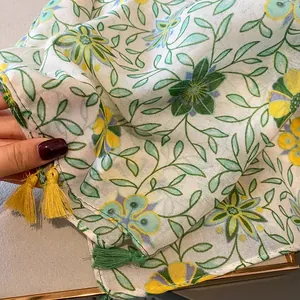 Dettaglio di sciarpa in cotone e lino con stampe floreali e nappe gialle decorative
