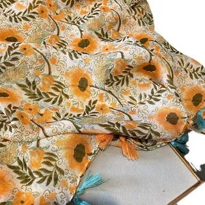 Floral print scarf with orange flowers and colorful tassels on light cotton-linen fabric