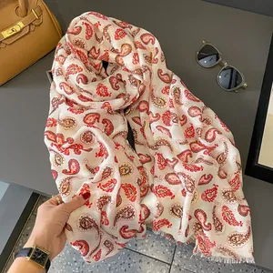 Dettaglio macro della stampa Paisley rossa e accenti dorati su sciarpa color crema