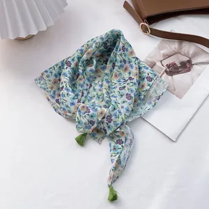 Lightweight floral cotton linen scarf with green tassels displayed on a white table