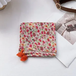 Close-up of floral print cotton linen scarf featuring orange pom-pom tassel details