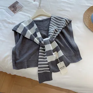Detail eines grauen Strickschals mit weiß gestreifter Krawatte und handgefertigtem Etikett