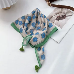 Detail of floral cotton linen scarf featuring blue flowers and green corner tassels
