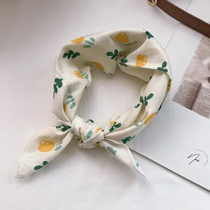Detailaufnahme eines Seidenschals mit gelben Blumen und grünen Blättern auf hellem Grund