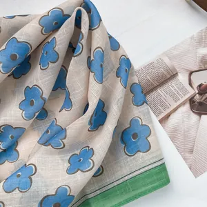 Detail of floral linen scarf showing blue flower patterns and green border texture