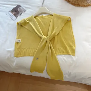 Detail of a bright yellow knitted shawl featuring a fine texture and decorative silver button