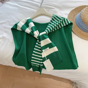 Detailansicht eines grün-weiß gestreiften Strickschals mit Markenetiketten auf dem Bett