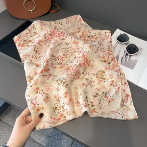 Detail of soft beige scarf featuring delicate pink floral prints and fine tassel edges