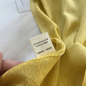 Detailed care label on yellow knit shawl showing 25% mugwort fiber and acrylic blend