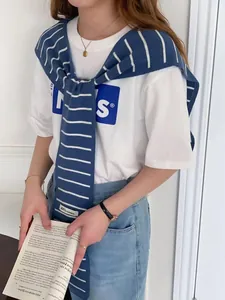 Détail d'un châle en maille rayée porté sur un t-shirt blanc décontracté