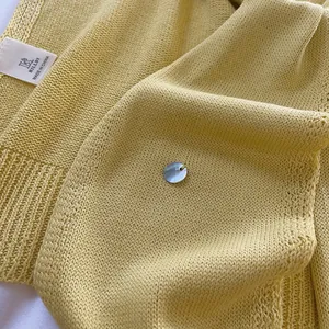 Detail of soft yellow knit fabric texture with a delicate button and woven brand label