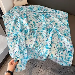 Close-up of lightweight white scarf with blue floral pattern and fine fringe edges