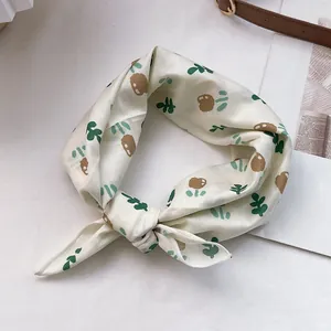 Nahaufnahme eines Seidenschals mit grünen Blättern und braunen Blumen auf creme Stoff
