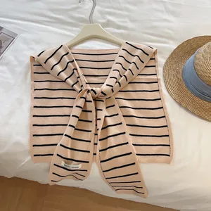 Détail d'un châle en tricot rayé avec nœud frontal sur cintre contre un drap blanc