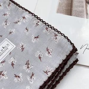 Macro detail of floral cotton scarf with dark brown lace trim and brand tag