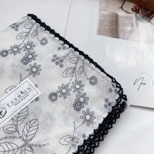 Detail of white cotton scarf with blue floral pattern and delicate crochet lace edging