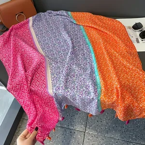 Détail d'une écharpe en coton et lin colorée avec motifs floraux et pompons orange