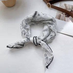 Close-up of a white cotton scarf with black floral prints and elegant crochet lace edges