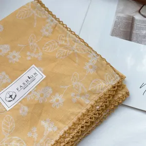 Detail of yellow floral cotton scarf featuring white print and delicate crochet lace trim