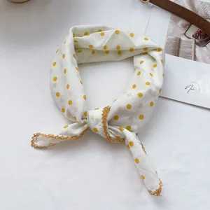 Detail of yellow polka dot square scarf with golden lace trim on white fabric background