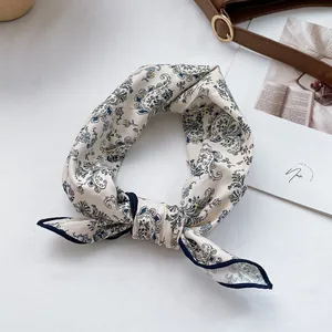 Detail of paisley floral cotton scarf in cream with blue border on a leather bag