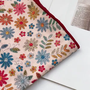 Détail macro de broderie florale sur coton beige avec bordure brodée rouge