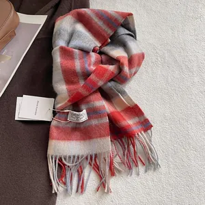 Detail of red and grey plaid 100% wool scarf featuring fringe tassels and brand label