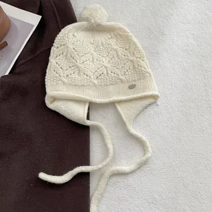 Close-up of beige wool hand-crocheted knit hat with fuzzy pom-pom and leaf-patterned texture