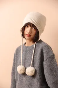 Detalle de gorro de lana crema con bordes acanalados y cordones con pompones en modelo