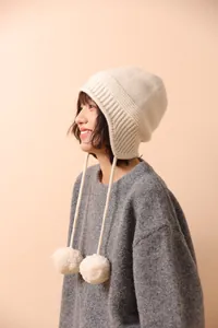 Textura de punto detallada de un gorro de lana crema con pompones y correas para las orejas