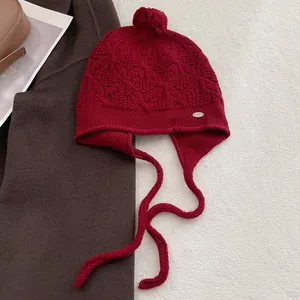Detail of burgundy wool knit earflap hat with diamond pattern and soft fur pompom