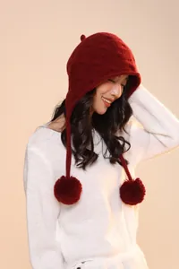 Detail of dark red knit wool trapper hat with fluffy pom-poms and warm ear flaps