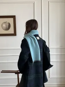 Detail of light blue wool blend scarf with fringe tassels worn over a plaid winter coat