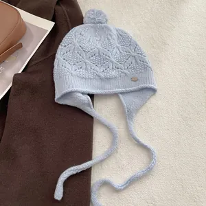 Close-up of light blue hollow-out crochet wool hat featuring a cute pompom and metal tag